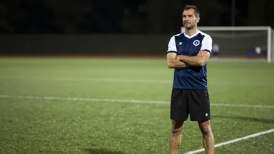 A 35-year-old, ruggedly-built, anonymous Derry City player, wearing a dark blue jersey with white sleeves and a white...
