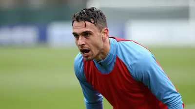 Mid-30s Derry City midfielder, athletic build, intense eyes, hair damp from training, captured waist-up in a plain red...