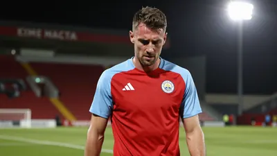 A concerned, athletic-built Derry City midfielder in his late 20s, wearing a plain red and sky blue training top, stands...