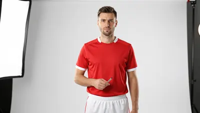A tight waist-up shot of a 30-40 year old male Derry City staff member, wearing a red jersey and white shorts, with a...