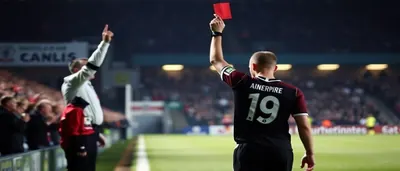 A Derry City player in plain white-and-red kit stands dejected on the pitch, head bowed, as empty red seats stretch...