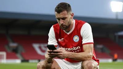 A tight action crop of an anonymous Derry City player, aged 30-40, wearing a red jersey with white sleeves and white...