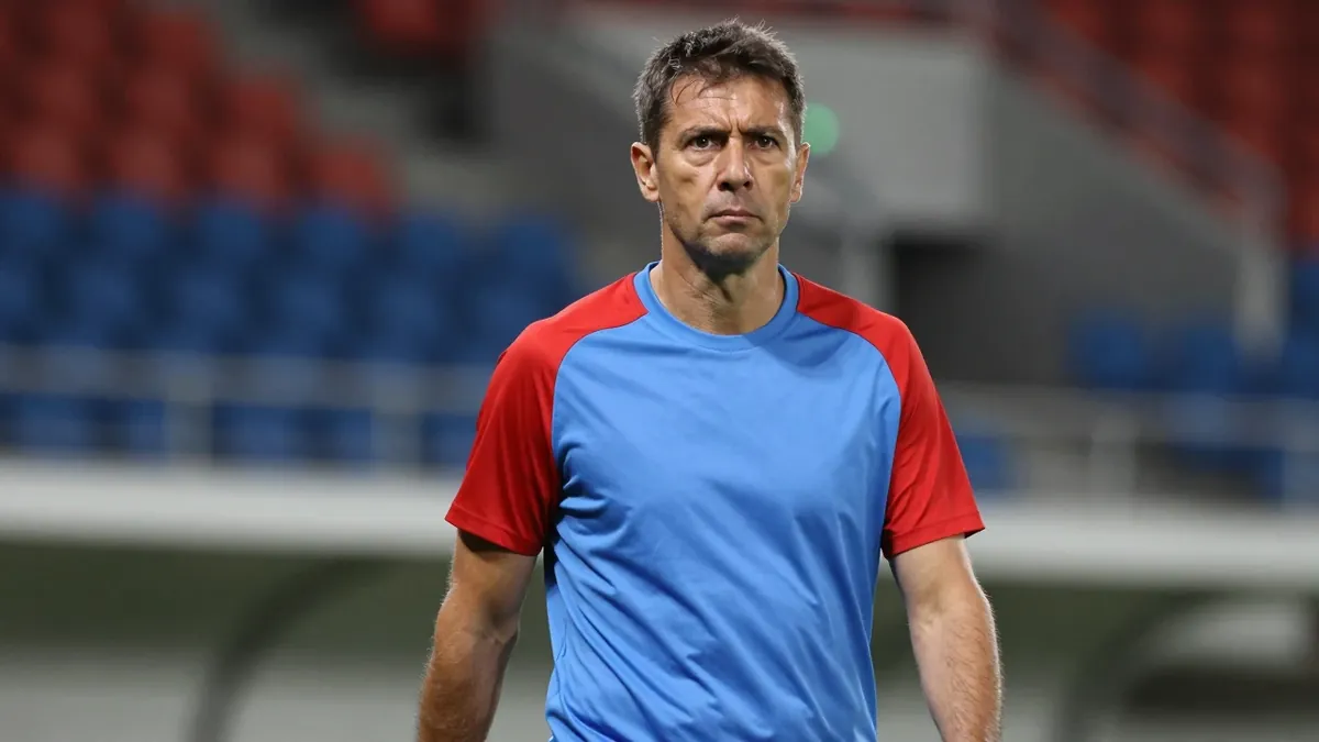 Middle-aged male coach, mid-40s, athletic build, waist-up, wearing a plain unmarked training top split red and sky-blue...